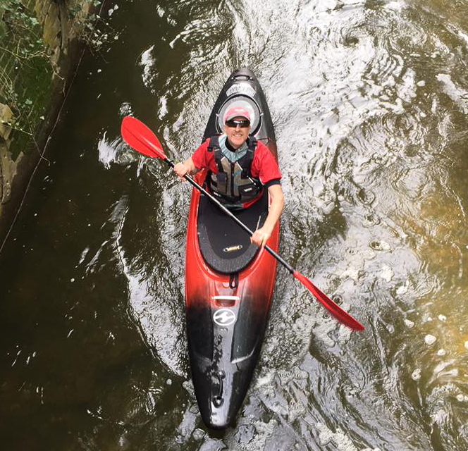 Person kayaking in red and black kayak on river, holding paddle.