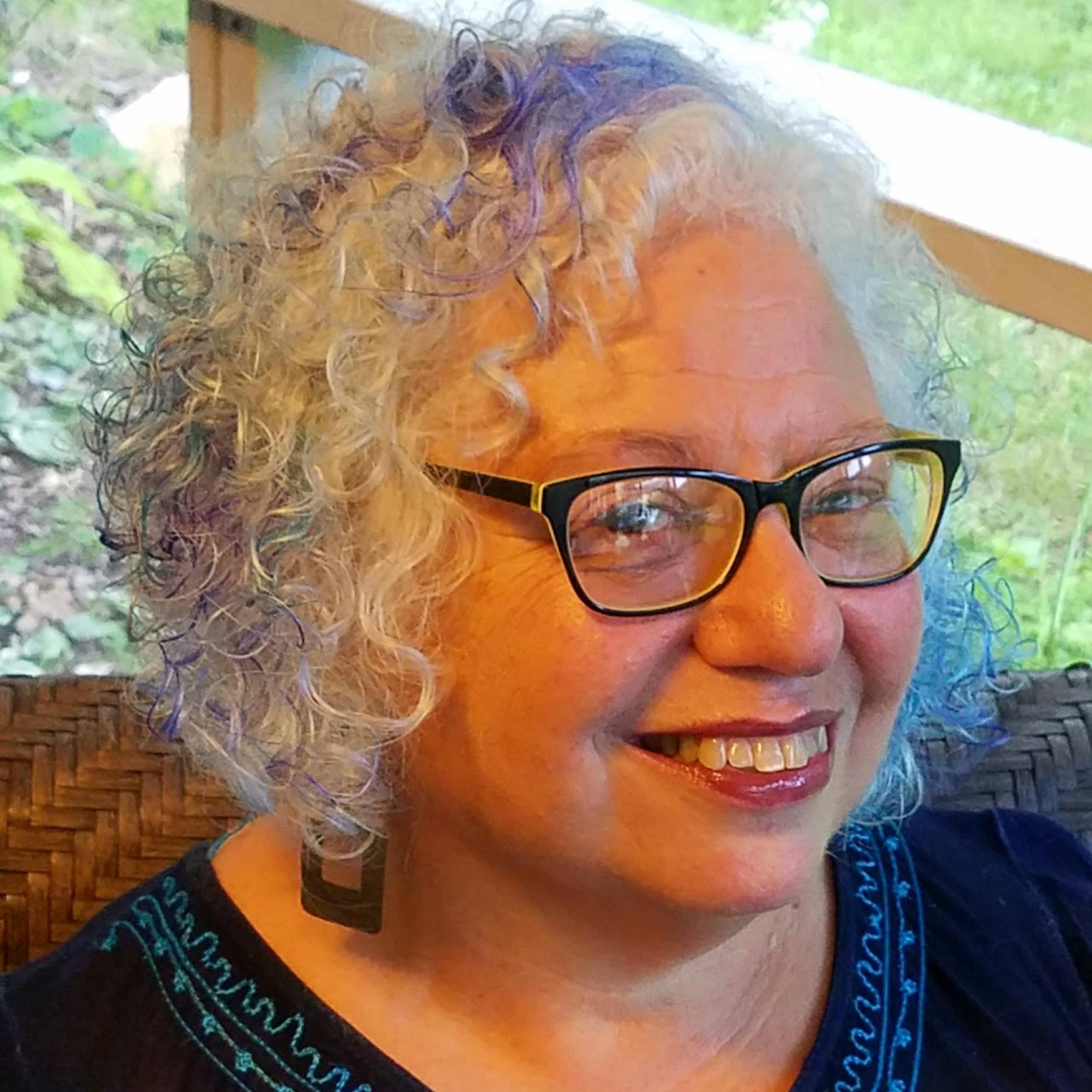 A woman with curly hair and glasses is smiling for the camera.