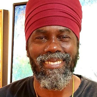 A man with a beard and a red turban is smiling.