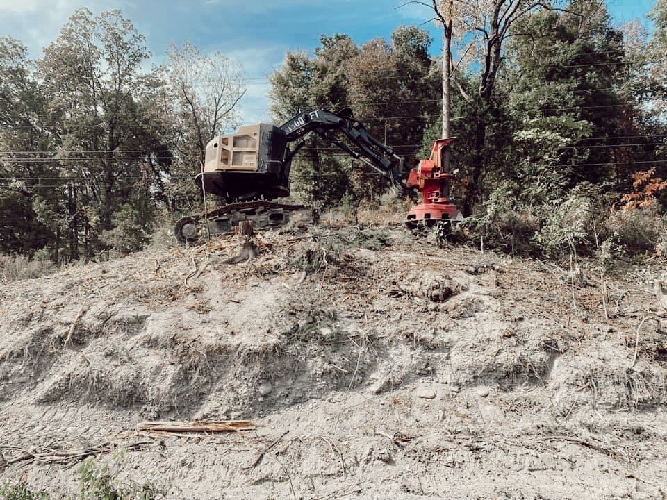 Excavator and red forestry machine working on a dusty hillside with trees in the background