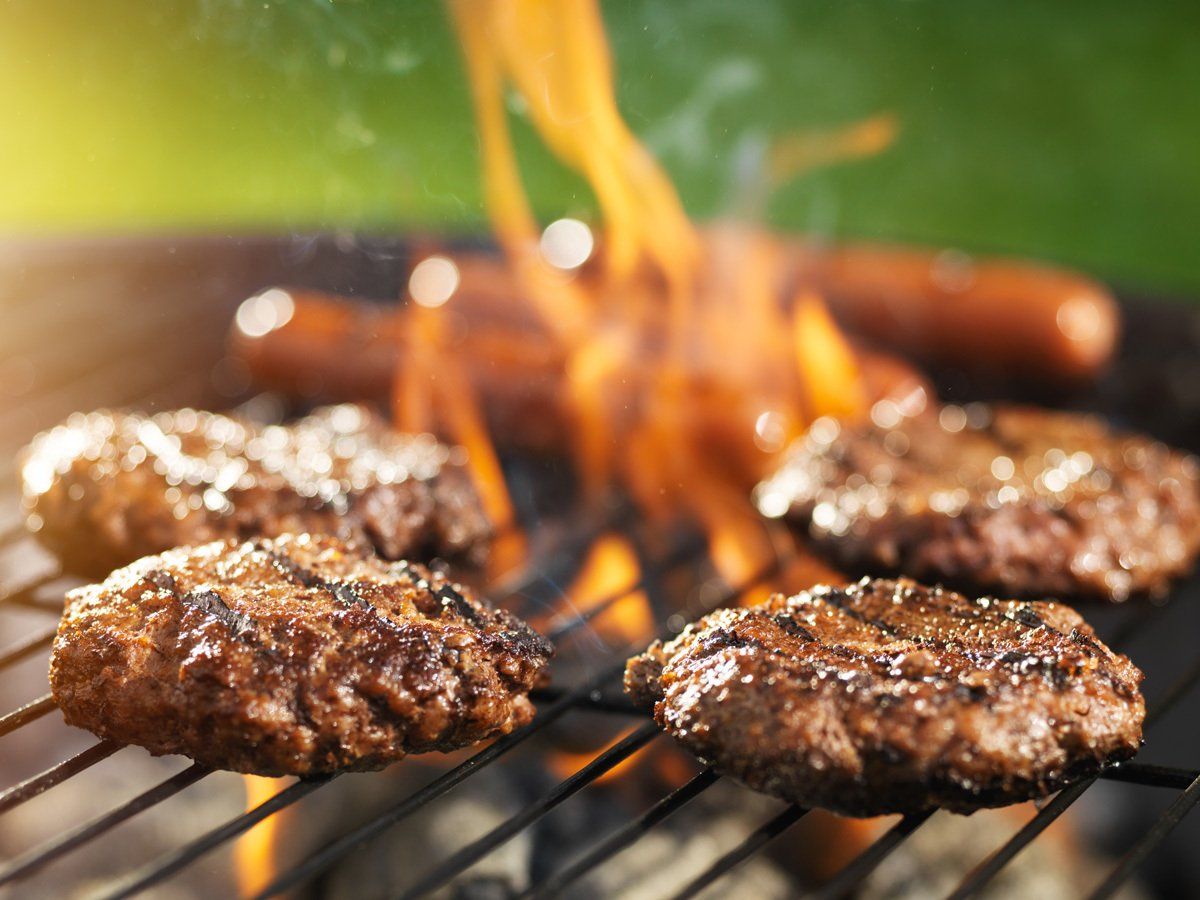 Hamburgers and hot dogs are cooking on a grill