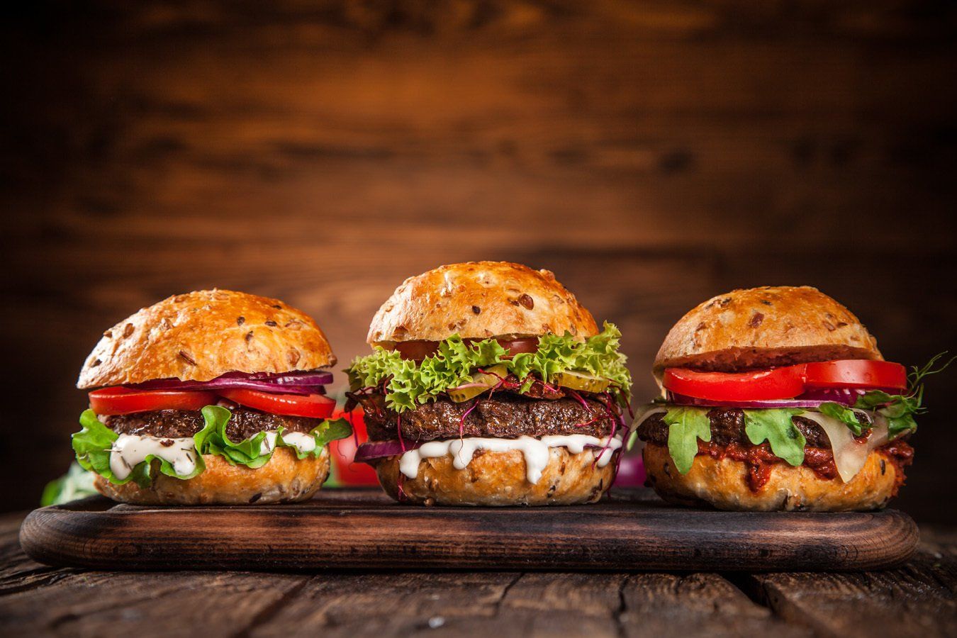 Three hamburgers are sitting on a wooden cutting board.