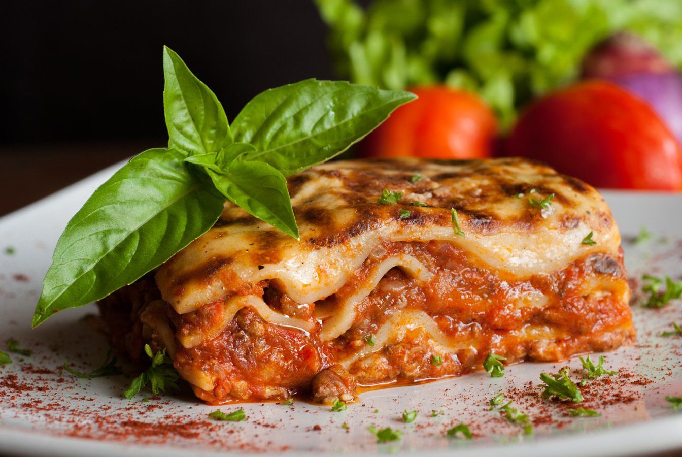 A white plate topped with a slice of lasagna and basil leaves.