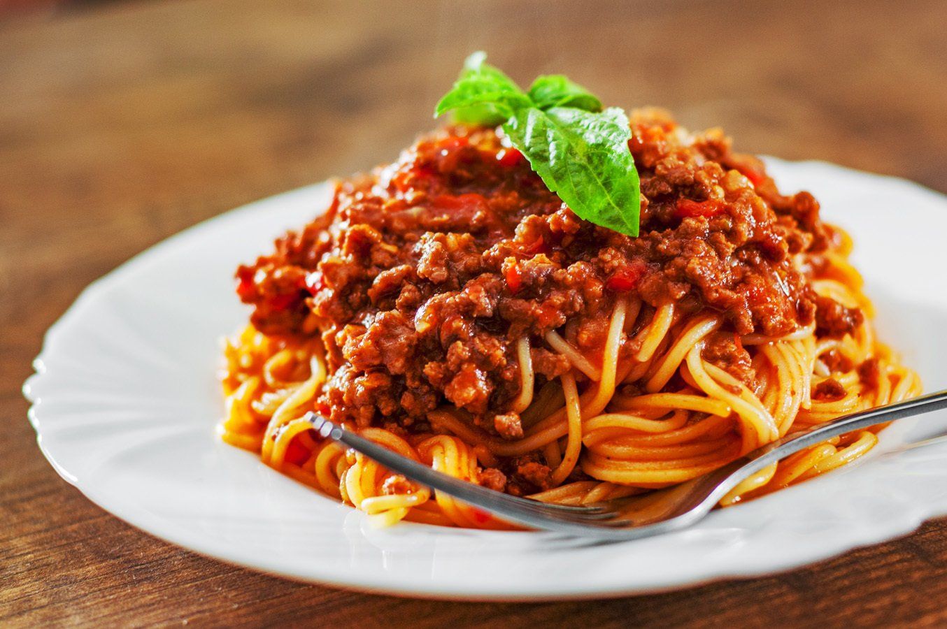 A white plate topped with spaghetti and meat sauce with a fork.