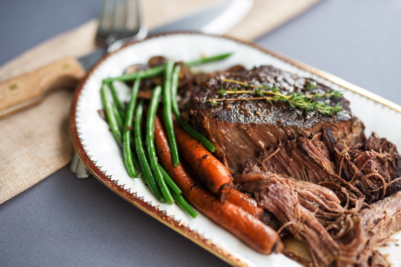 A plate of food with meat , carrots and green beans on a table.