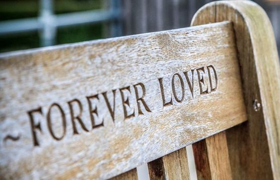Wooden memorial bench engraved “FOREVER LOVED” in a blurred outdoor setting