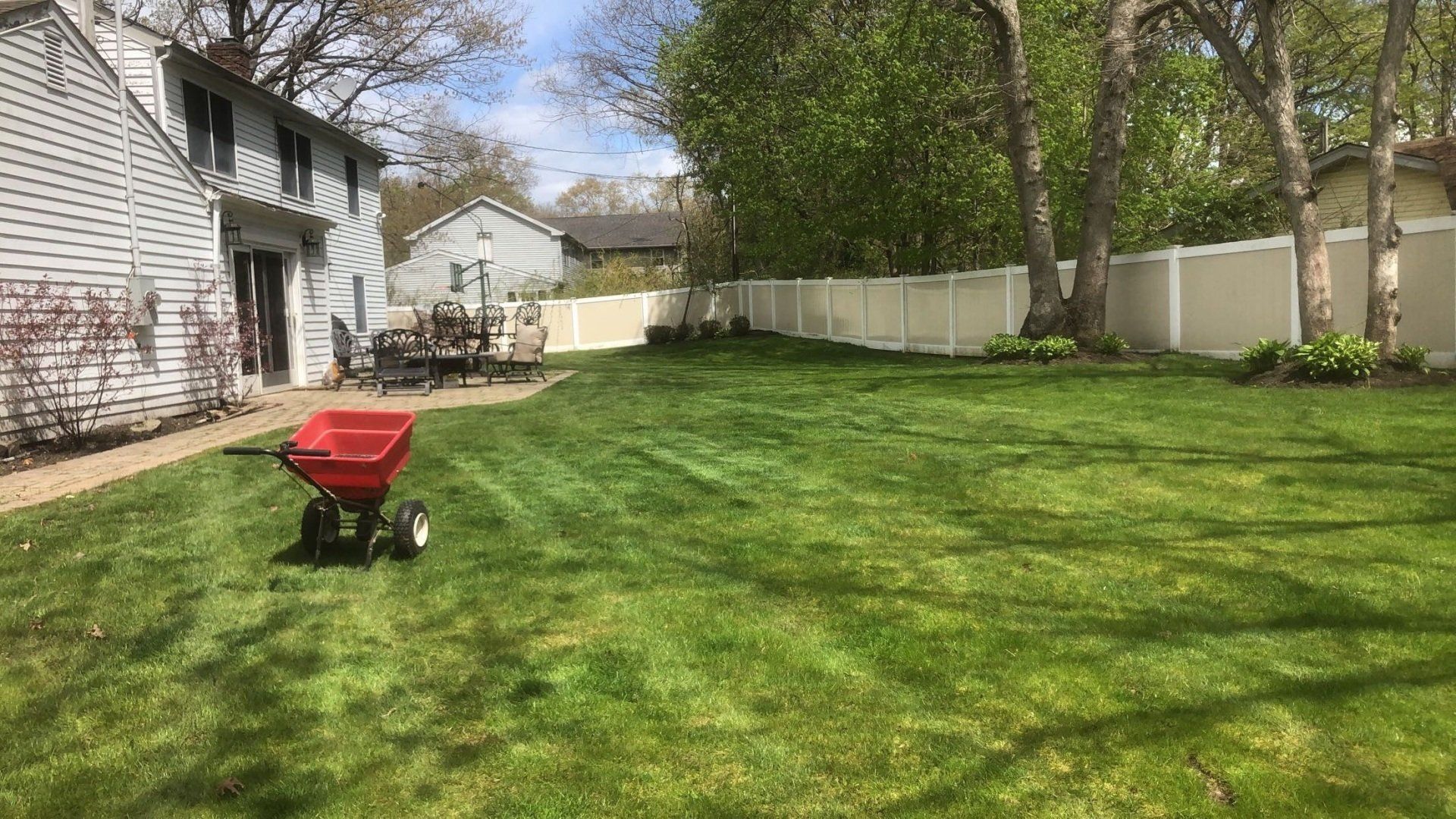 A red spreader is sitting in the middle of a lush green lawn.