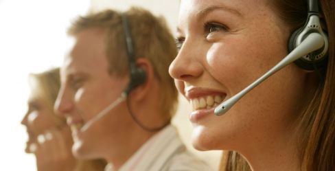 Three customer service agents wearing headsets, smiling in a call center.