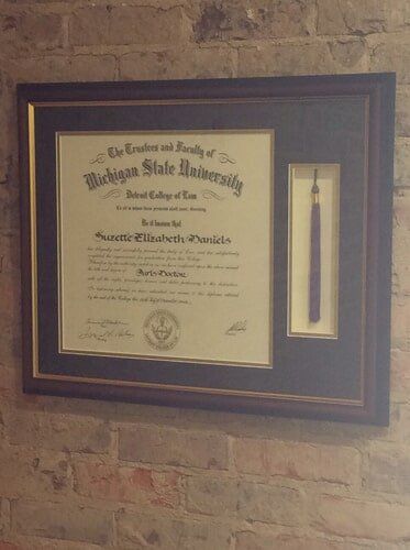 Framed Michigan State University diploma and tassel on a brick wall.
