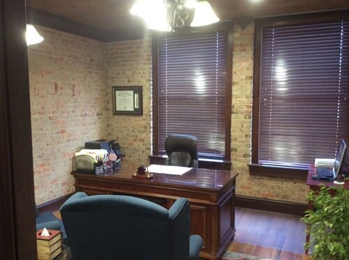 Office with exposed brick walls, wooden desk, blinds, and blue chairs.