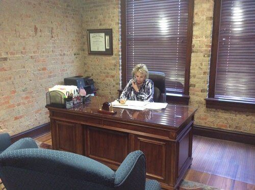 Woman at desk in office, talking on phone, brick wall backdrop.