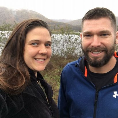 Smiling couple outdoors by a lake with misty hills in the background