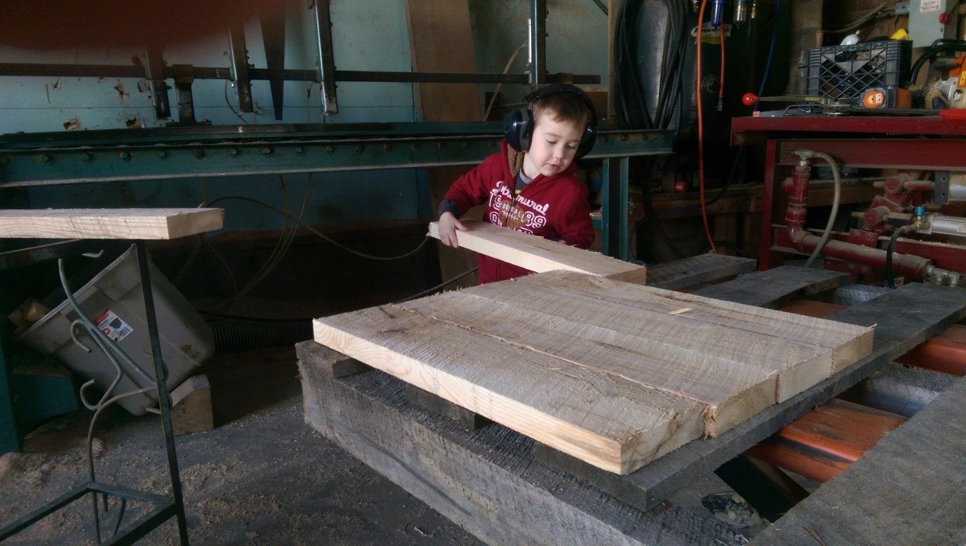 Person in a workshop leaning on a large wooden tabletop beside industrial machinery.