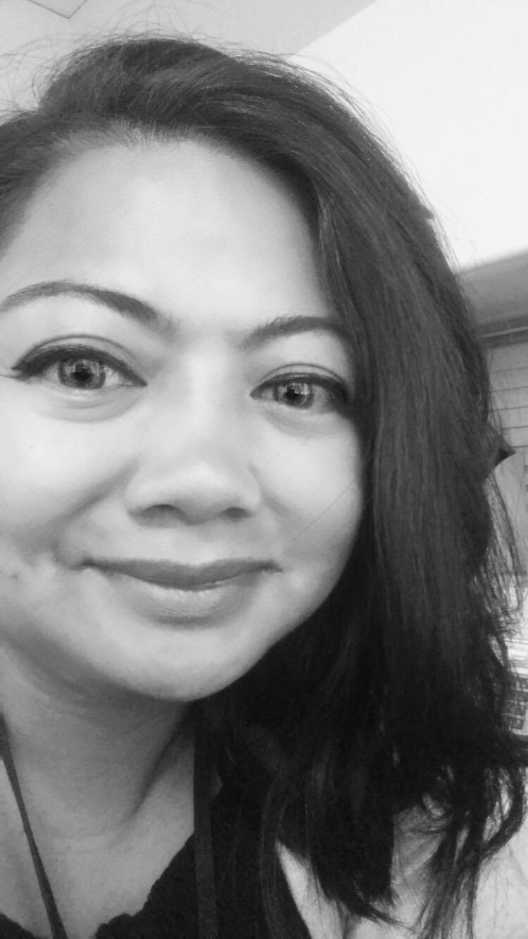 Close-up selfie of a smiling person with long dark hair, indoors, in black-and-white.