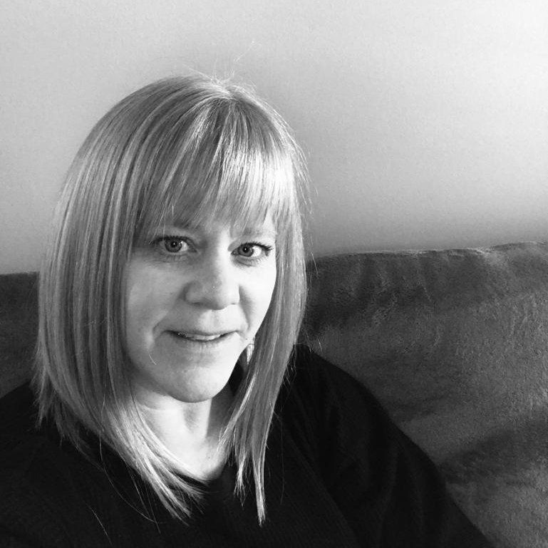 Woman with straight hair smiling on a couch in a black-and-white portrait