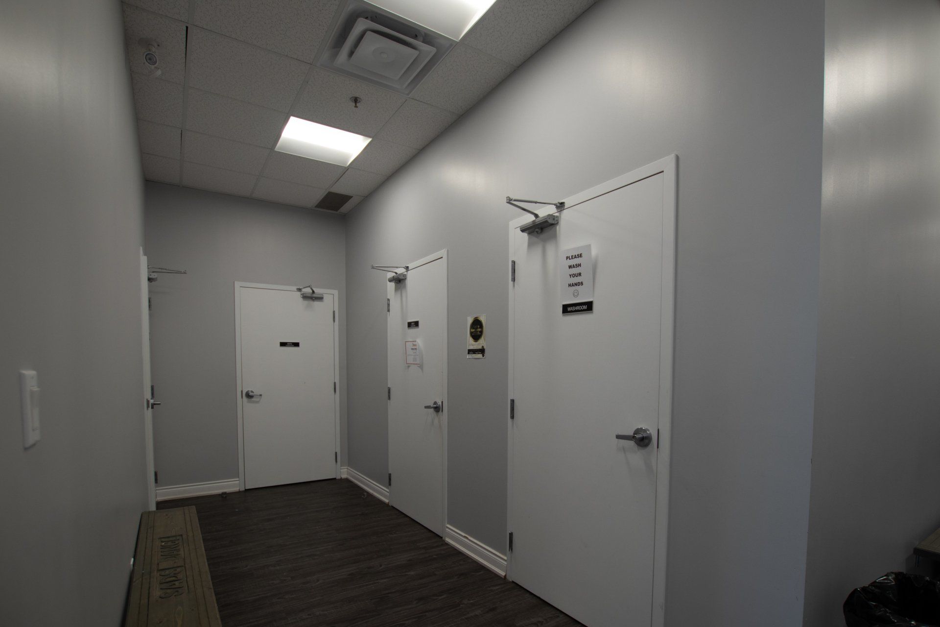 Narrow gray hallway with several white doors and overhead fluorescent lights