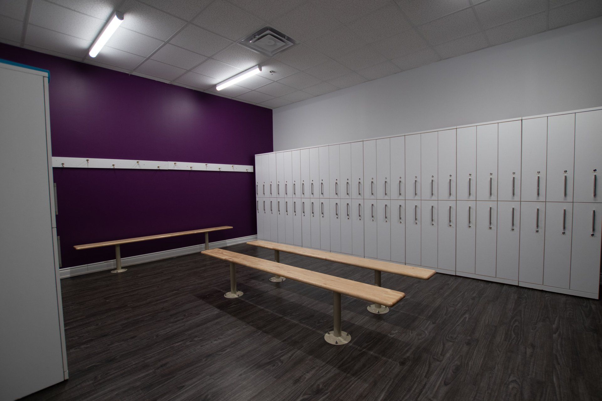 Locker room with white lockers, purple wall, and a wooden bench on dark carpet.