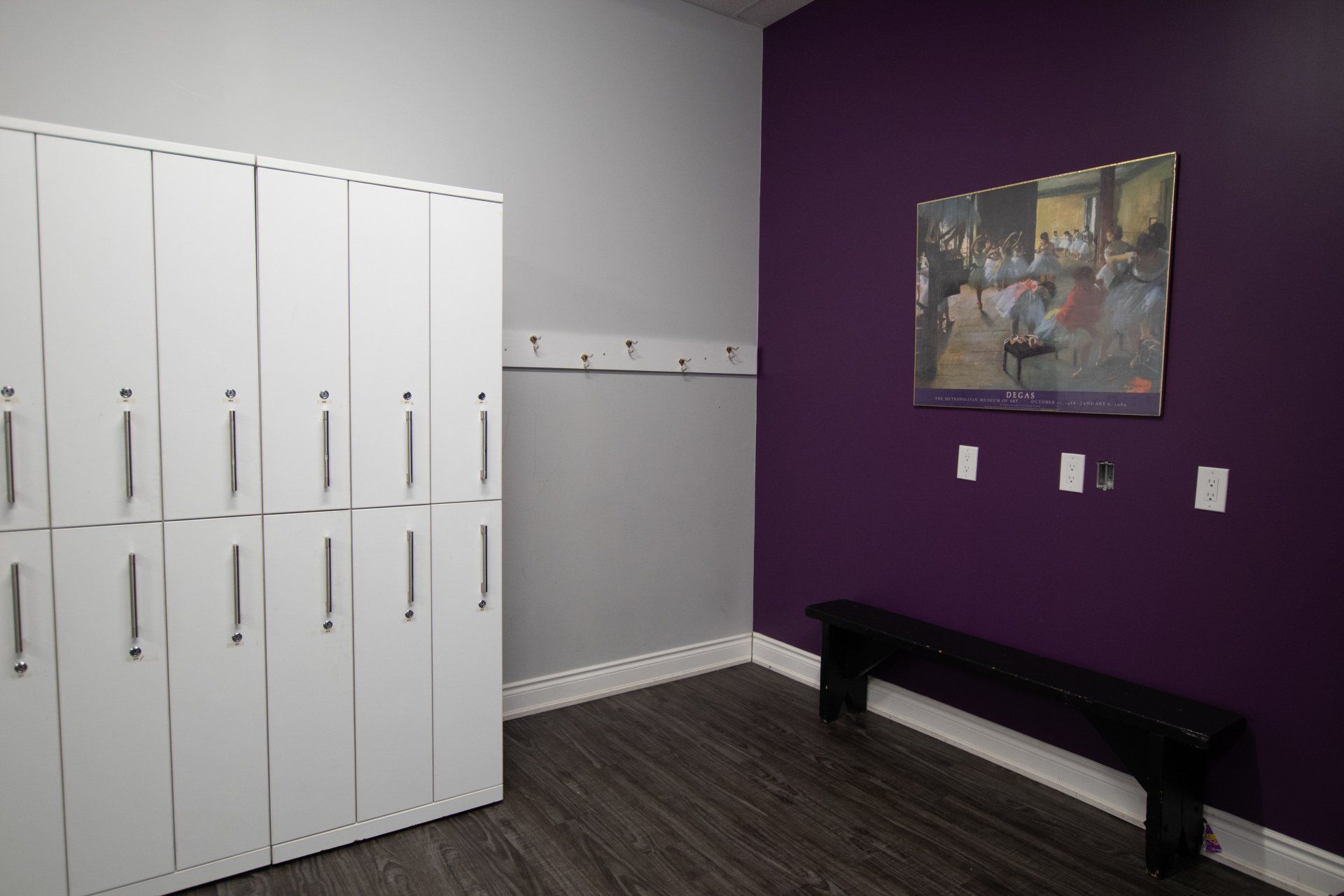 Purple locker room with white lockers, wall hooks, a bench, and framed artwork on the wall
