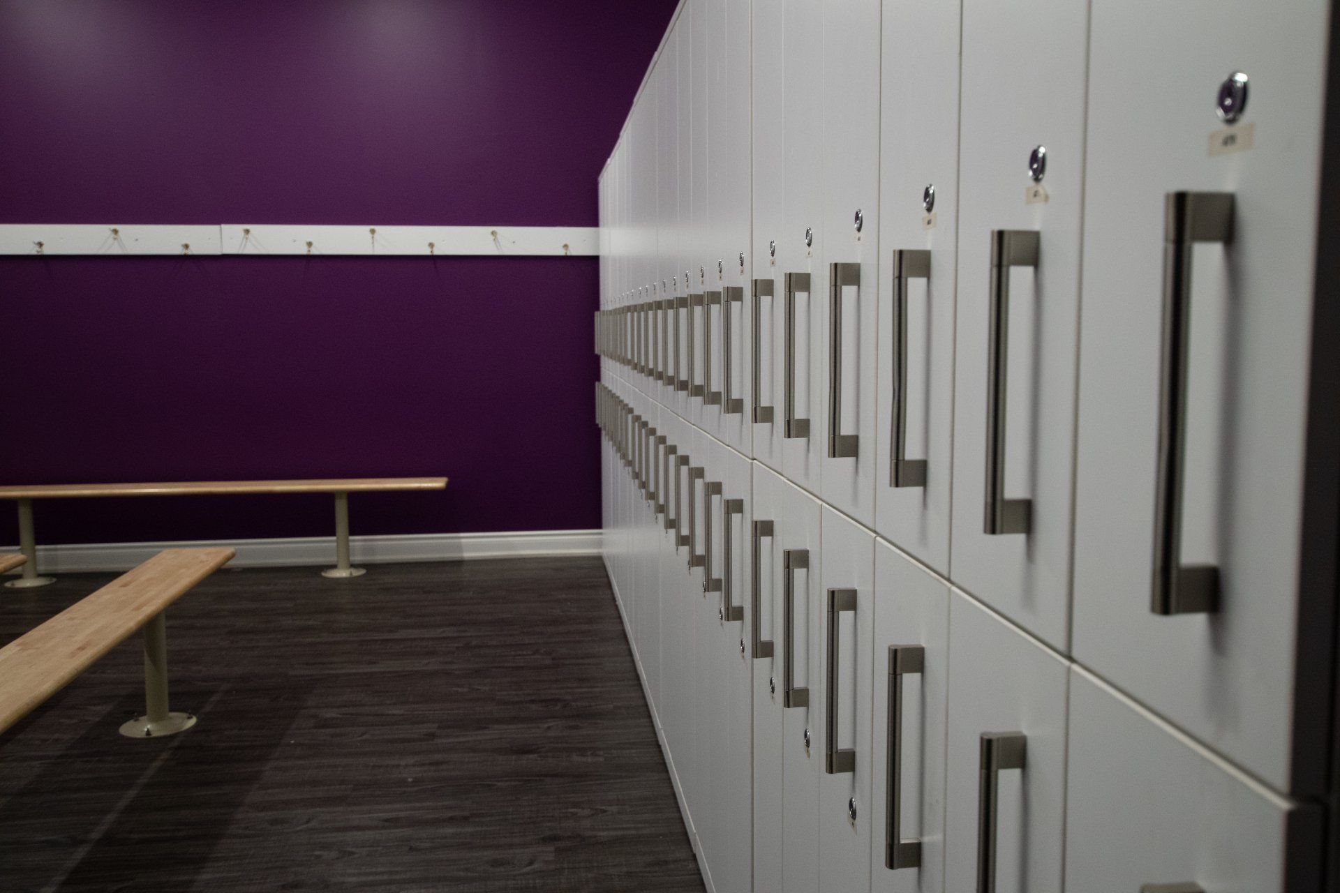 Row of white locker cabinets beside a purple wall in a locker room