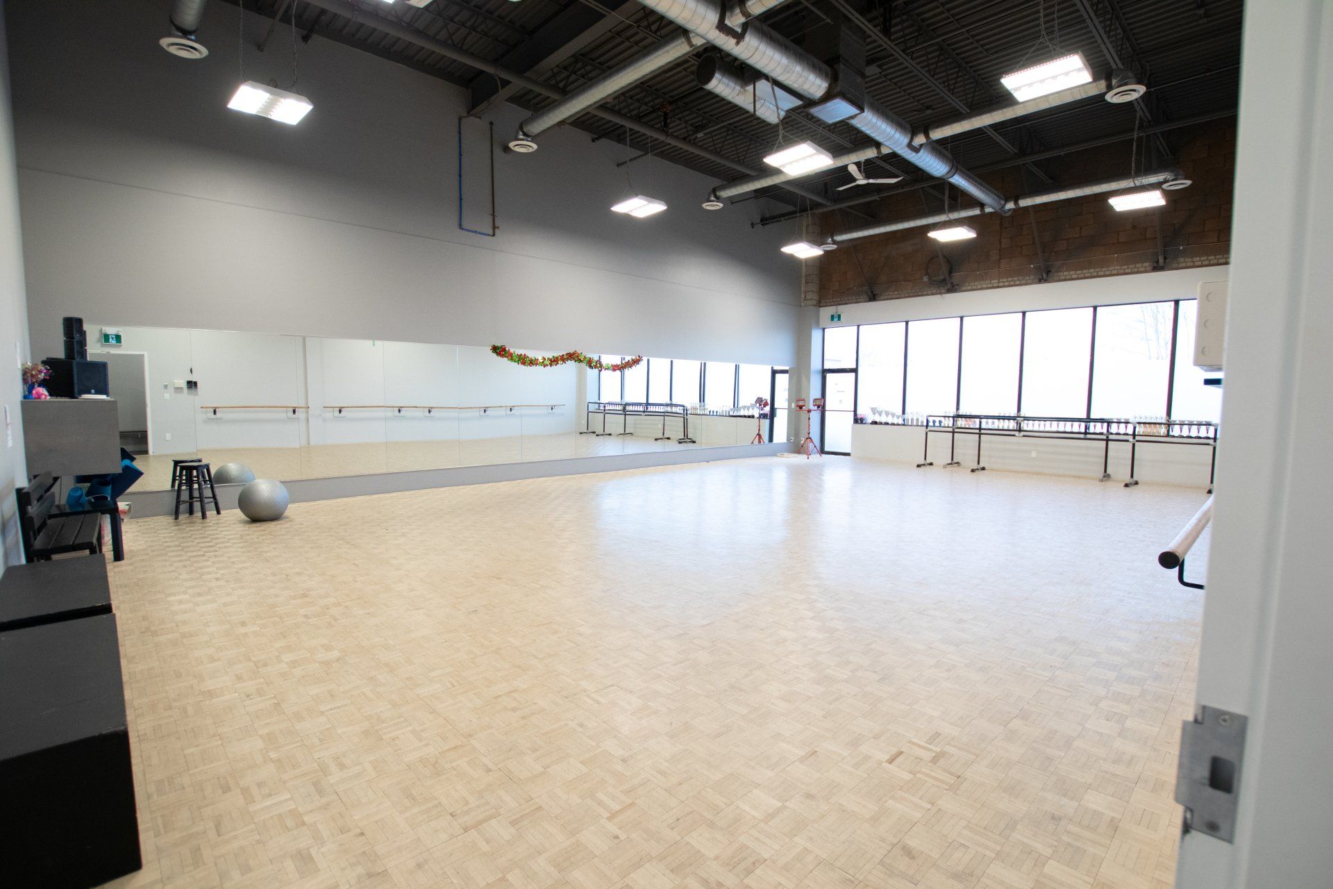 Empty bright studio with wood floor, mirrored wall, and large windows