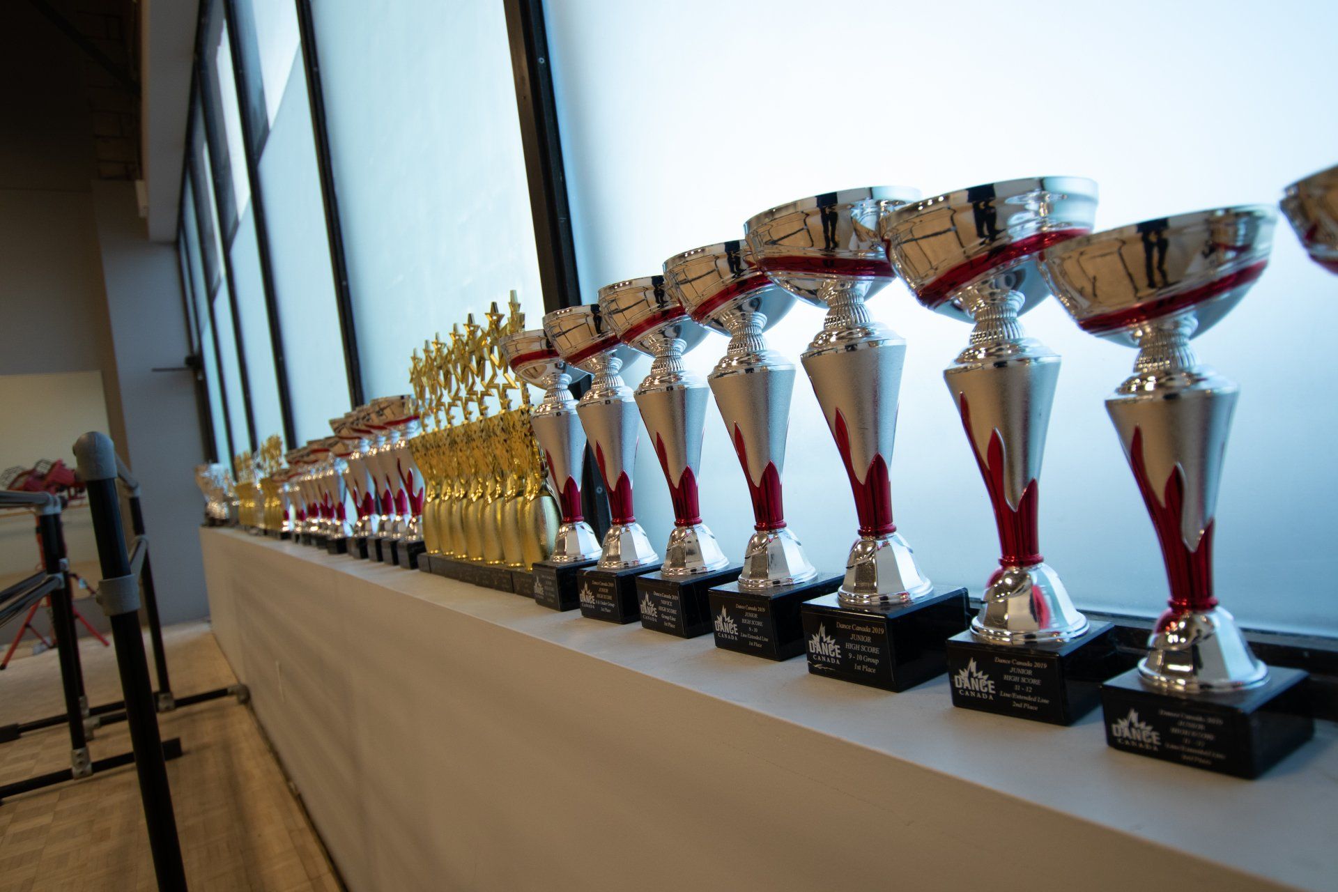 Trophy display on a long table with rows of silver and gold awards in a bright room