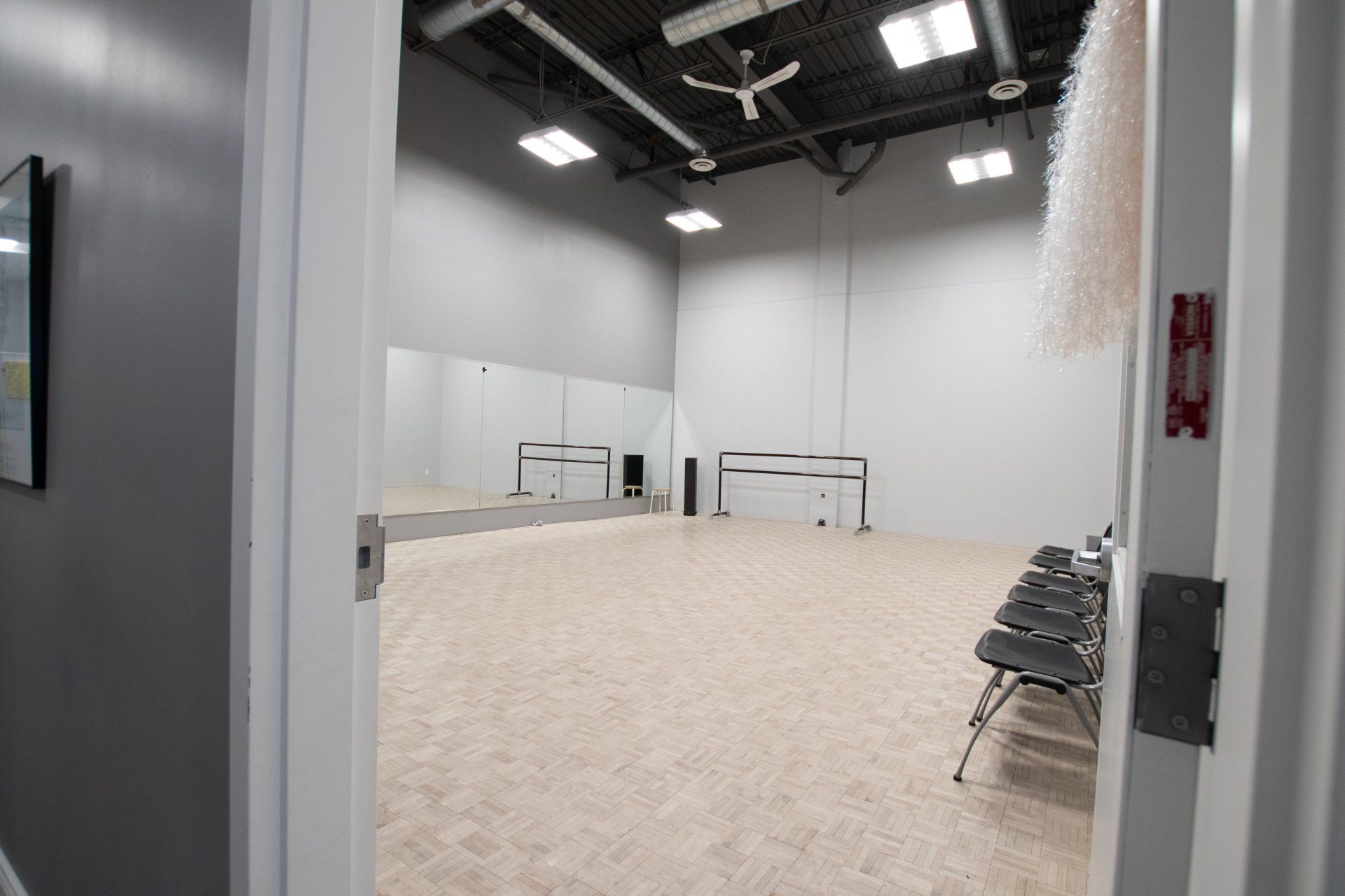 Empty dance studio with mirrors, beige floor, and stacked chairs along the wall