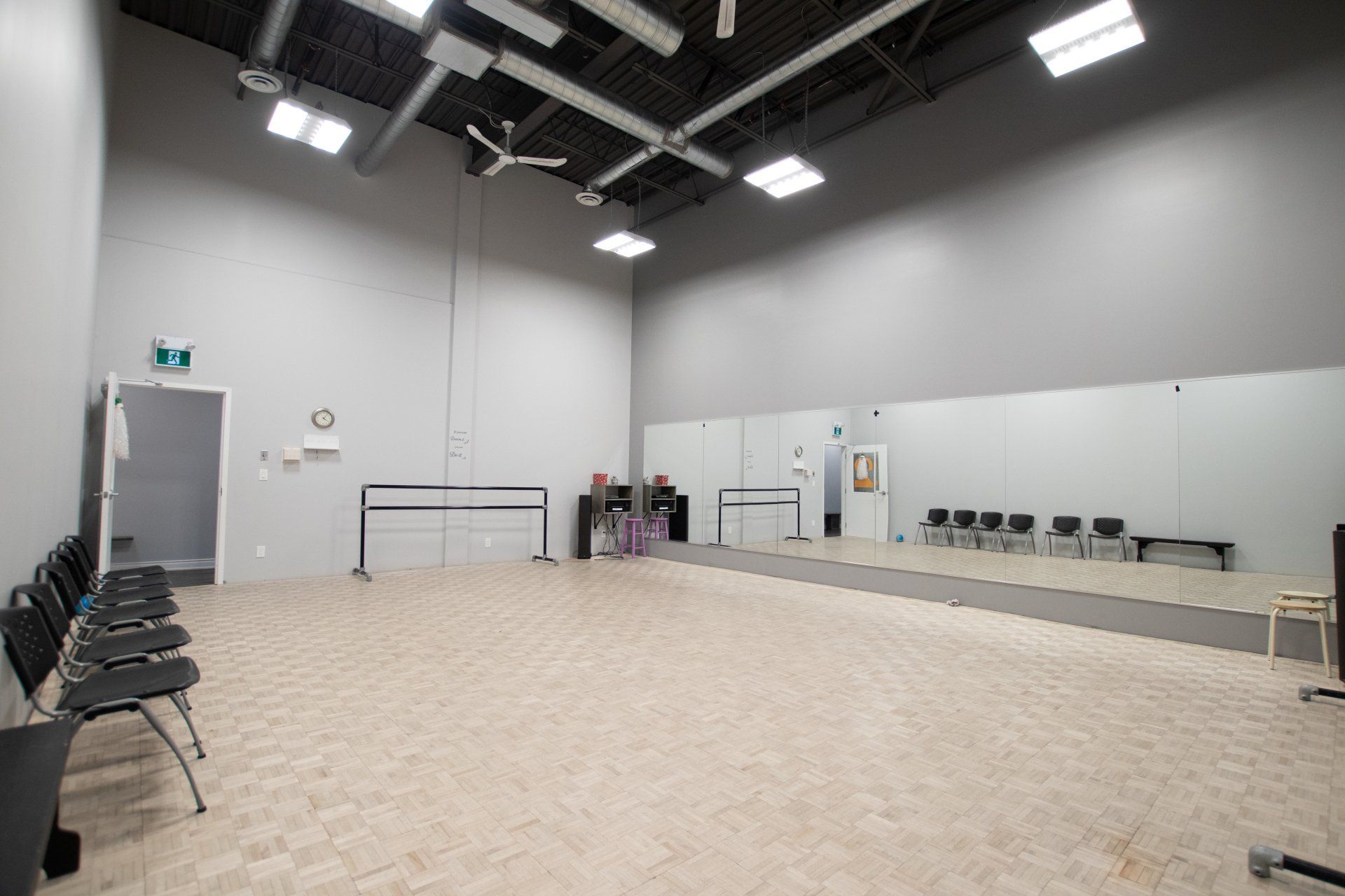 Empty dance studio with mirrors, chairs, overhead lights, and a beige floor