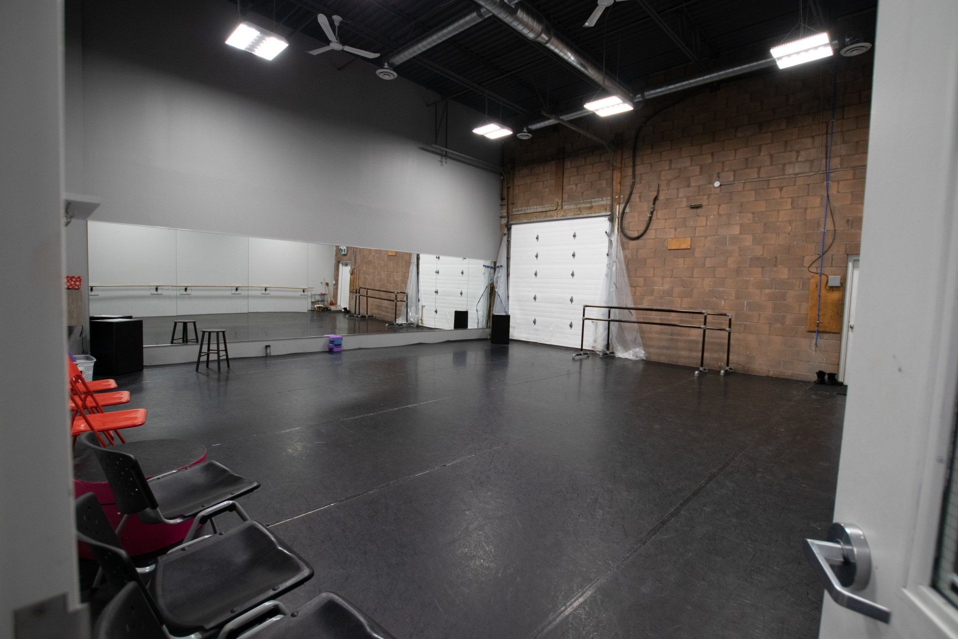 Empty studio room with black floor, folding chairs, whiteboards, and exposed brick wall