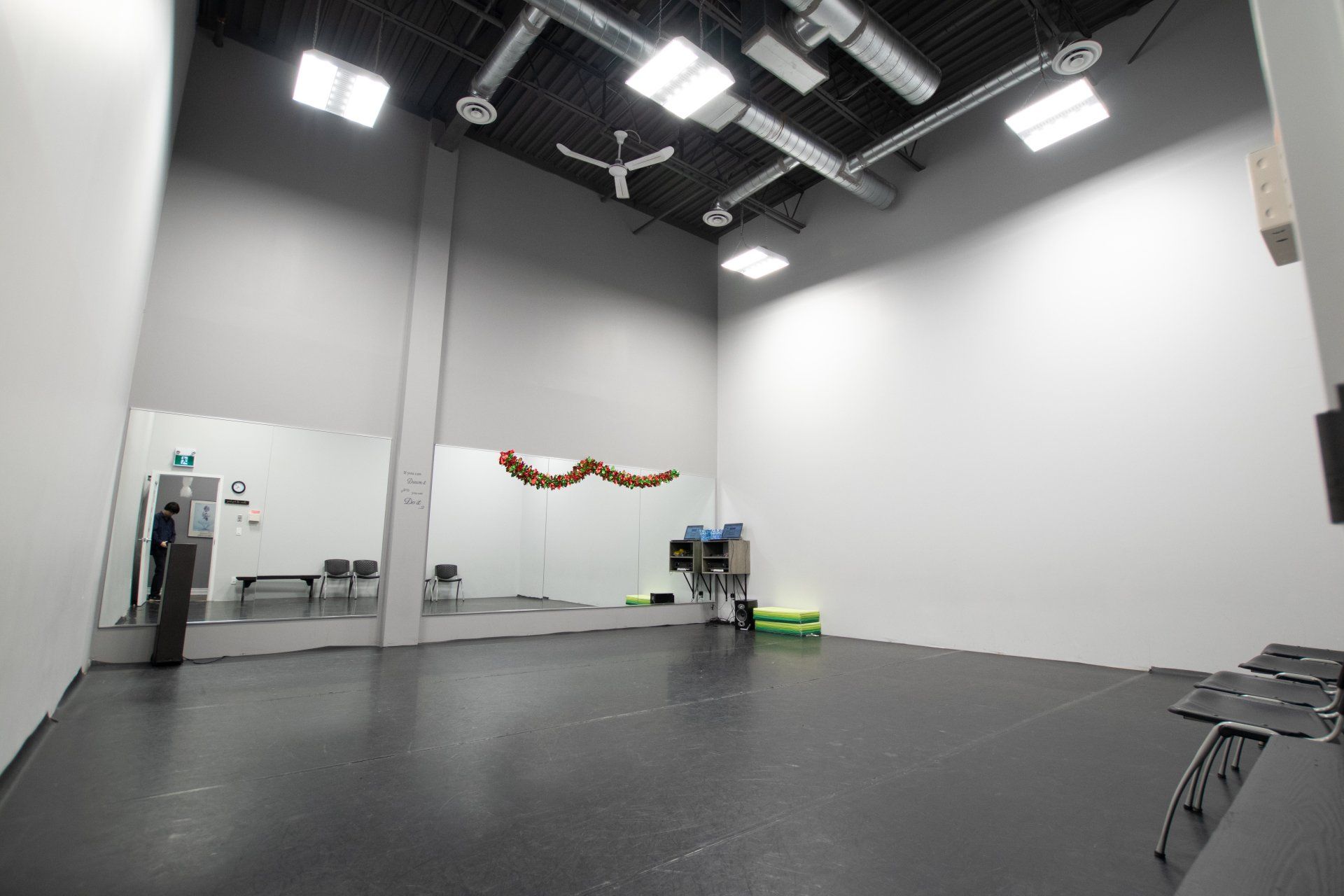 Empty dance studio with gray walls, black floor, mirrors, and ceiling lights