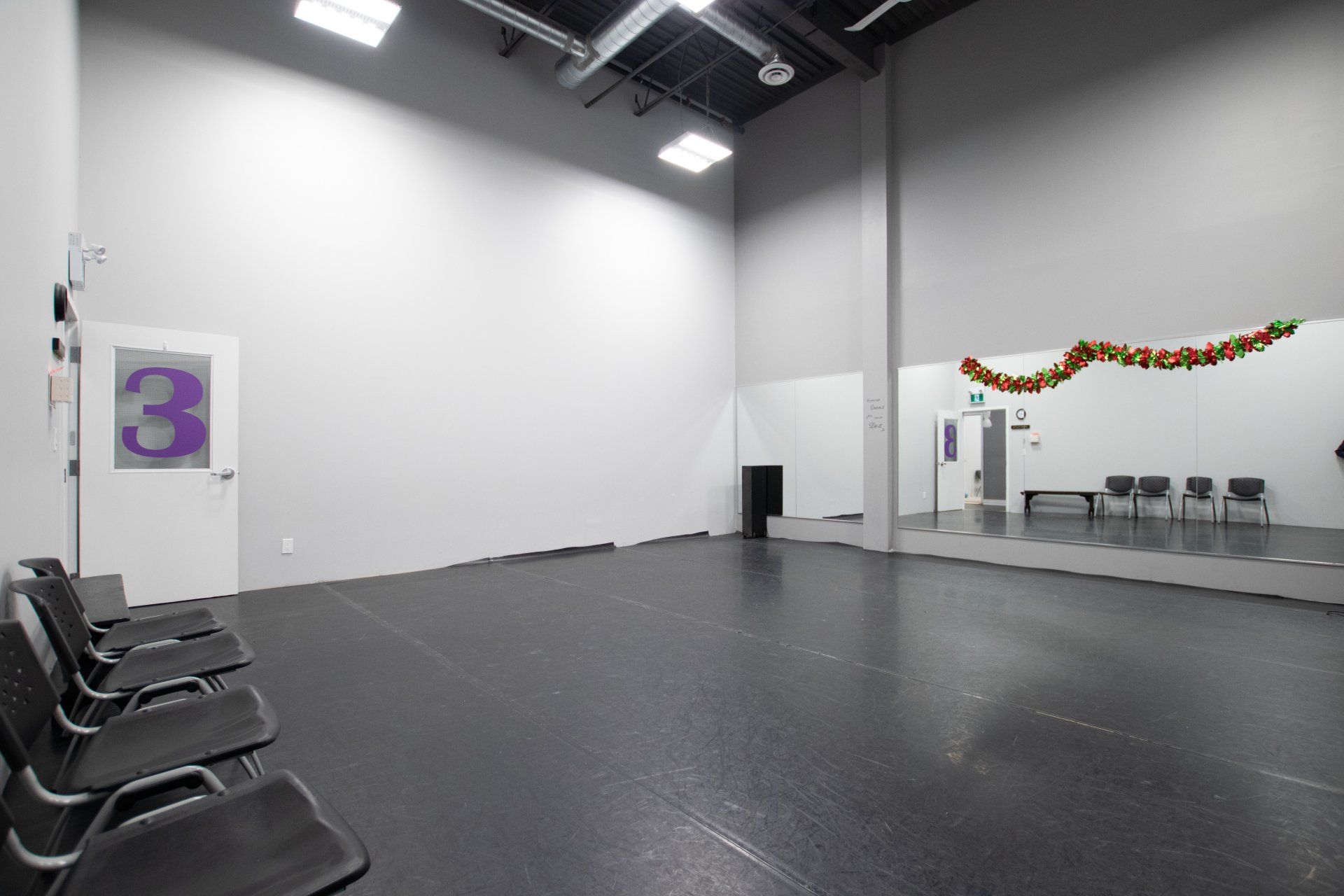 Empty indoor hall with rows of black chairs, white walls, and a purple number 3 sign