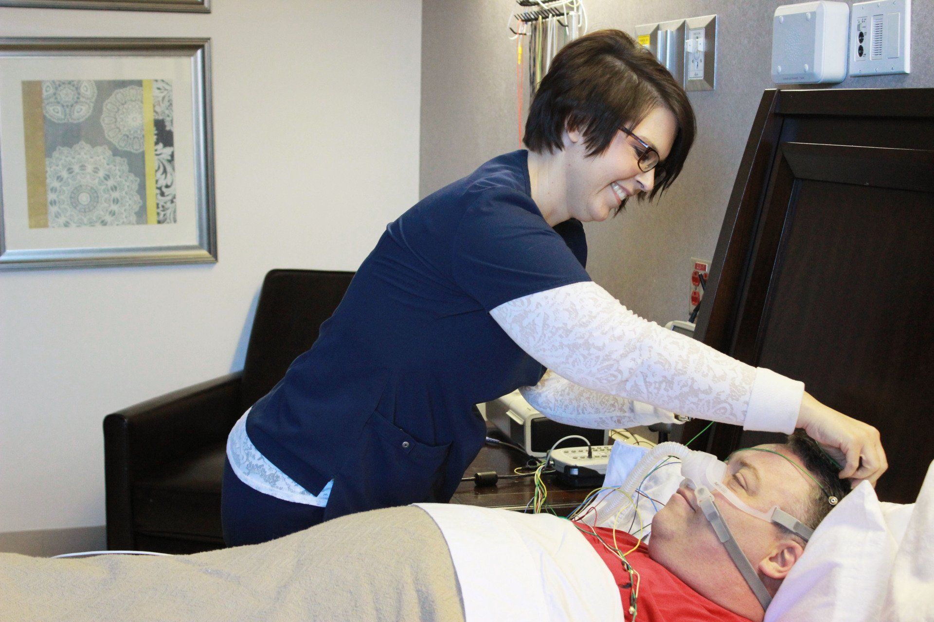 Nurse adjusts equipment on a patient in a hospital room.
