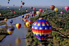 A bunch of hot air balloons are flying over a river.