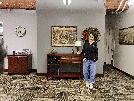 A woman is standing in a room with a clock on the wall.