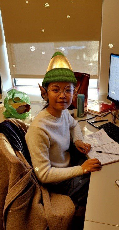 A woman wearing a green elf hat is sitting at a desk.
