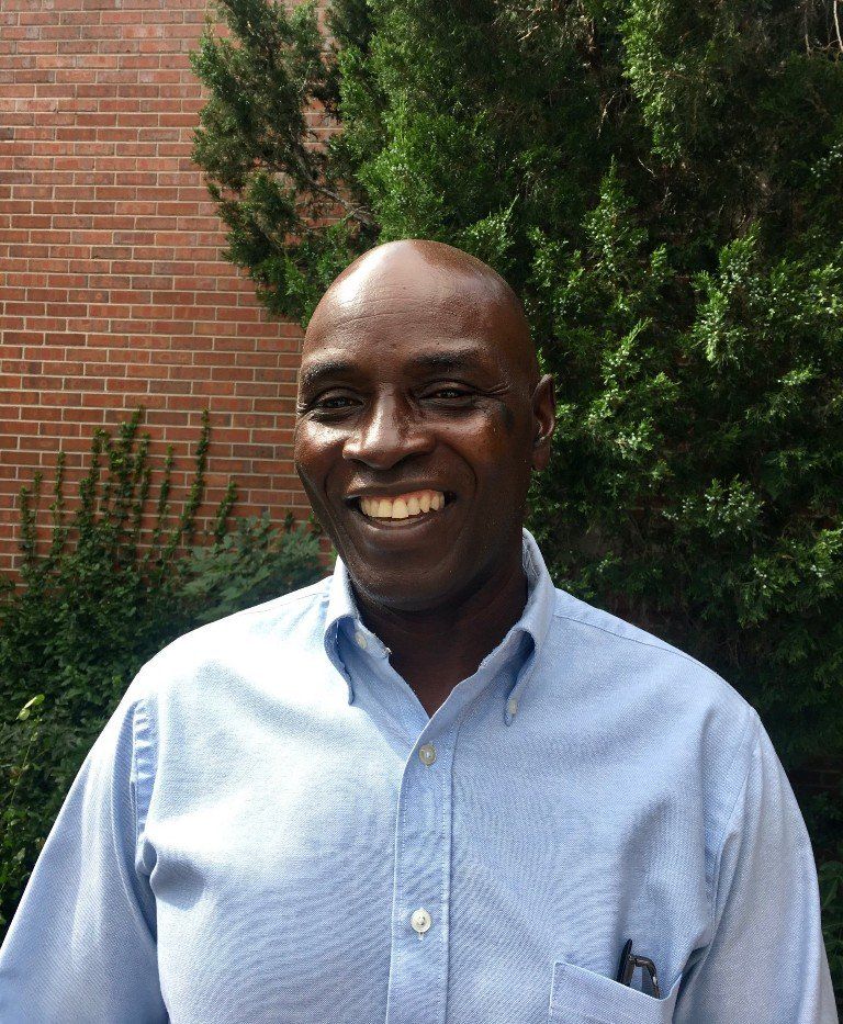 A cheerful photo of Patrick Lutalo wearing a blue shirt, displaying a warm smile.