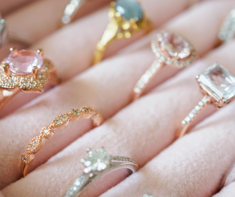Assorted rings with gemstones displayed on a hand, including pink, blue, and clear stones.