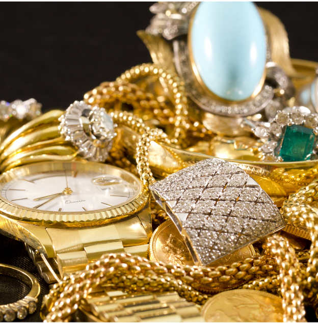 Gold jewelry and watches piled together, featuring a diamond-encrusted bracelet and gemstone rings