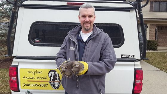 Man in gray jacket holding a small dog in front of a white van with an animal rescue sign