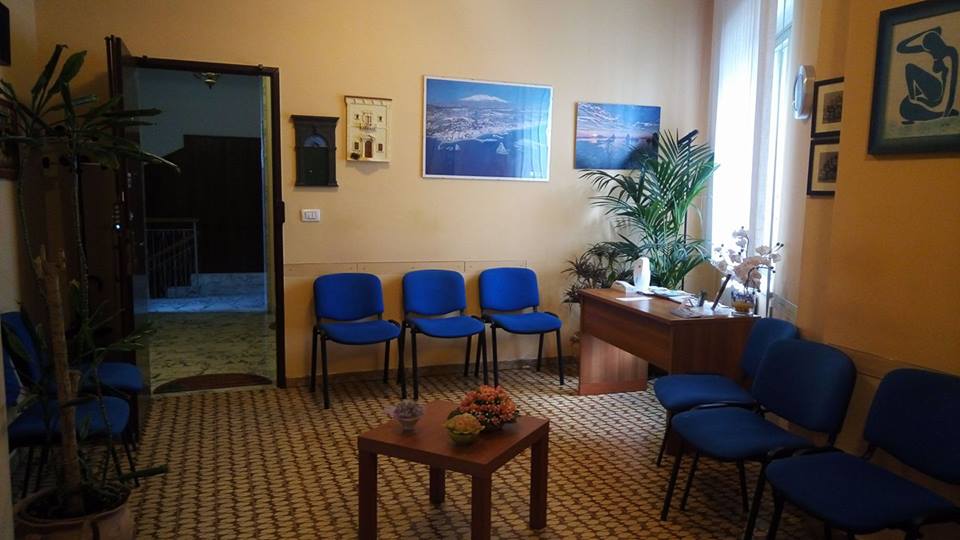 una sala d’attesa con delle sedie blu e sulla destra una scrivania marrone
