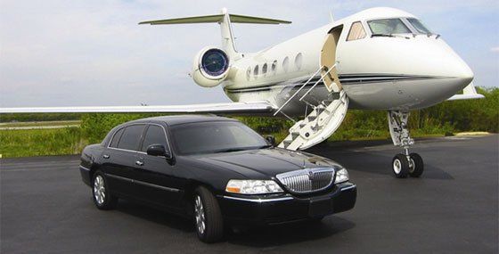 Black limousine in front of a white private jet, on a tarmac. The jet's door is open.