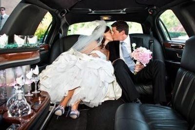 Newlyweds kissing in the back of a black limousine. Bride in a white dress, groom holding a bouquet.