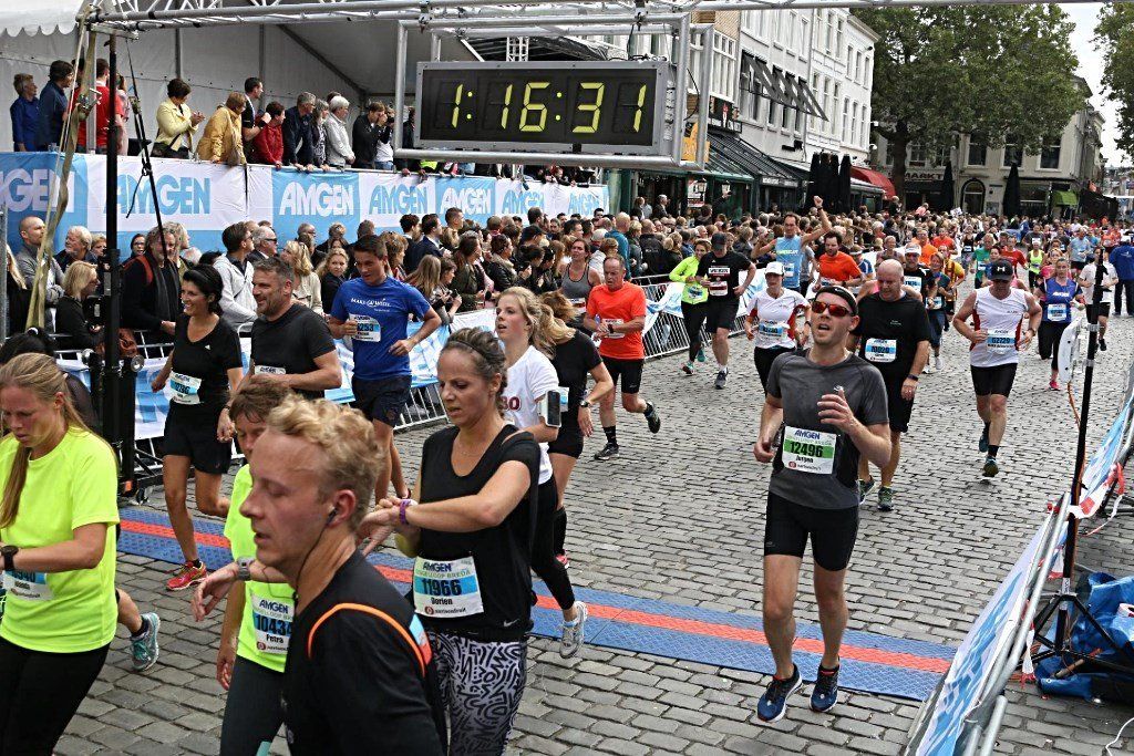 Hardlopers in een wedstrijd, met een digitale tijdwaarneming die 1:16:31 aangeeft, omringd door een menigte langs de straten.
