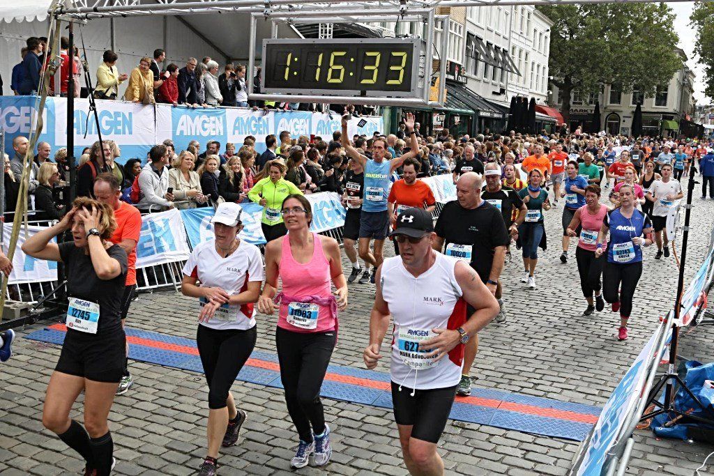 Hardlopers passeren de finishlijn, de timer geeft 1:16:33 aan. Publiek op de achtergrond.