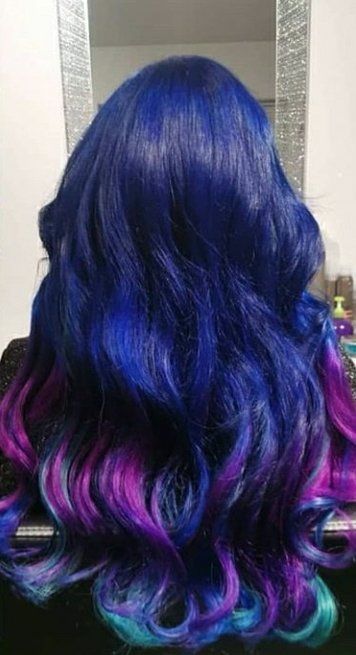 A woman with blue and purple hair is standing in front of a mirror.