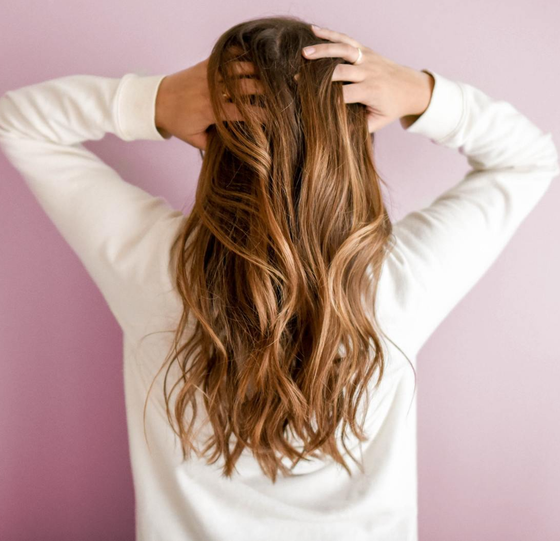 A woman in a white sweater is holding her hair in her hands.