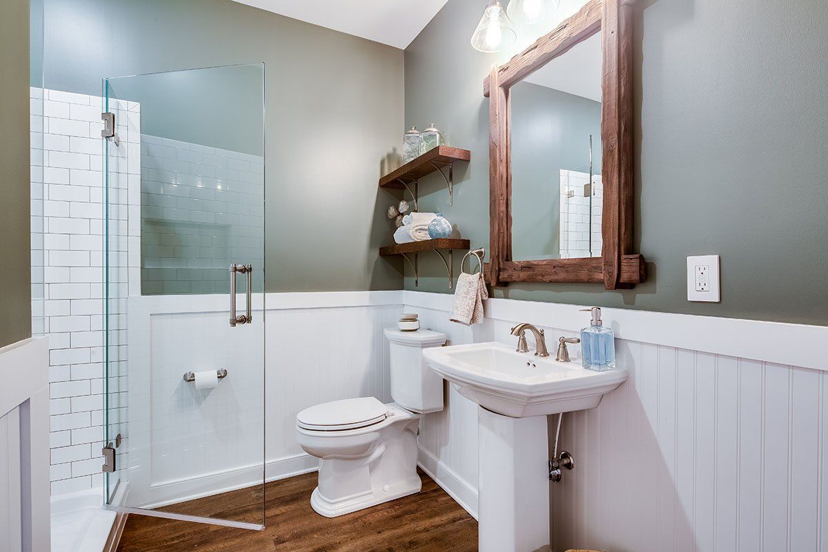 A bathroom with a toilet , sink , mirror and walk in shower.