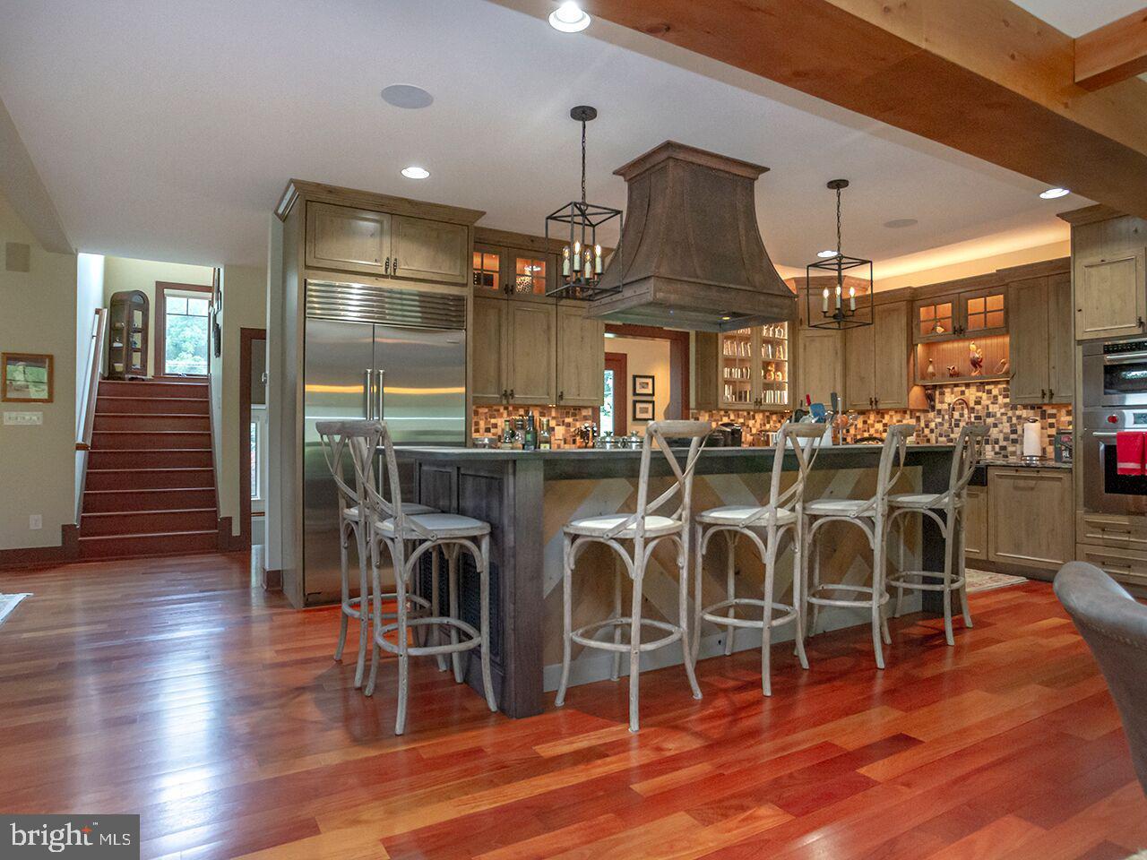 A kitchen with hardwood floors , stools and a large island.