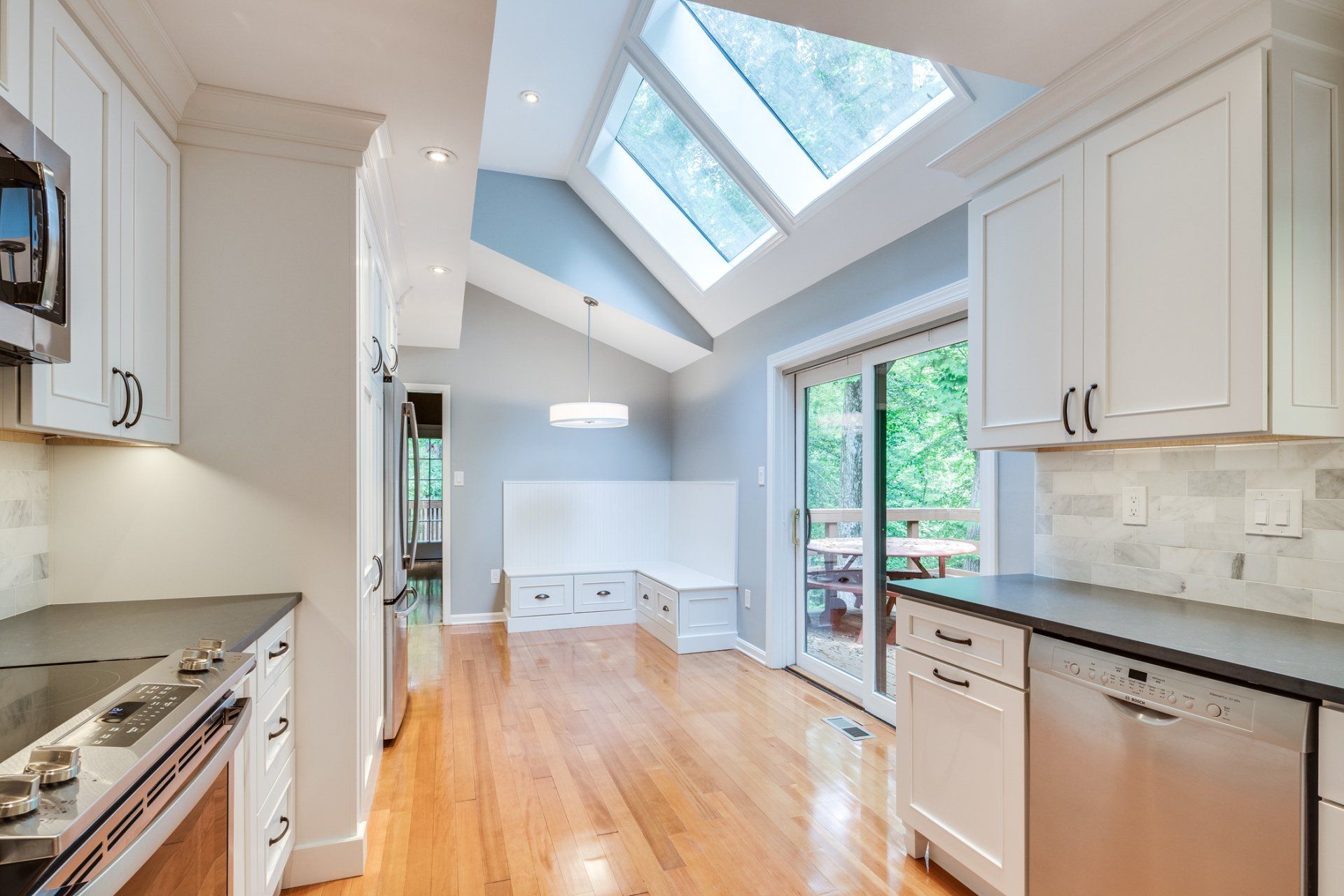 A kitchen with white cabinets , stainless steel appliances , hardwood floors and a skylight.