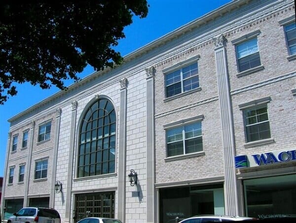 A multi-story building featuring a large arched window, tall decorative columns, and white brick facade.