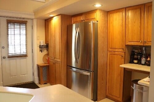 A kitchen featuring a stainless-steel refrigerator, natural wood cabinets, a white door with blinds, and a counter area.